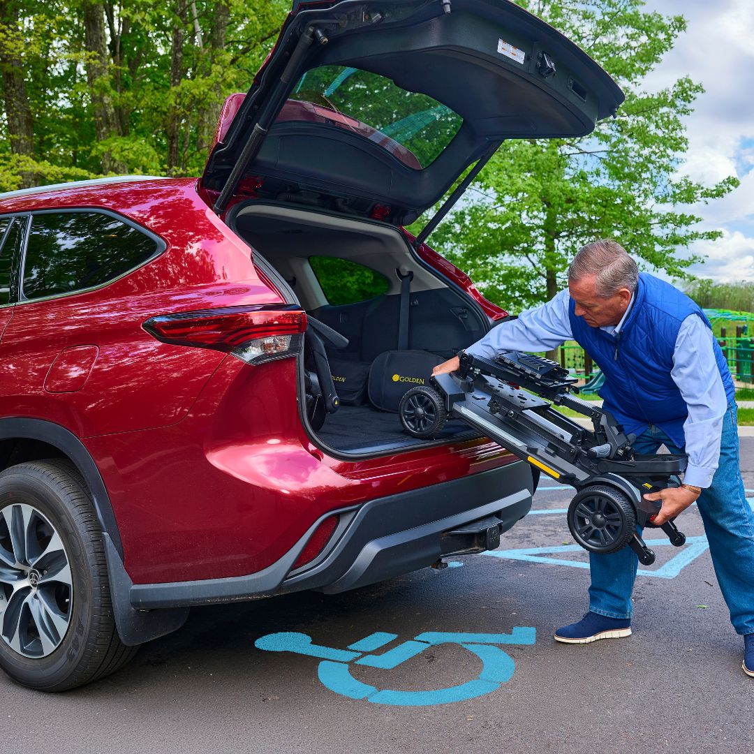 Man loading a CarryOn HD GB220 mobility scooter into the trunk of a red SUV with trees in the background.