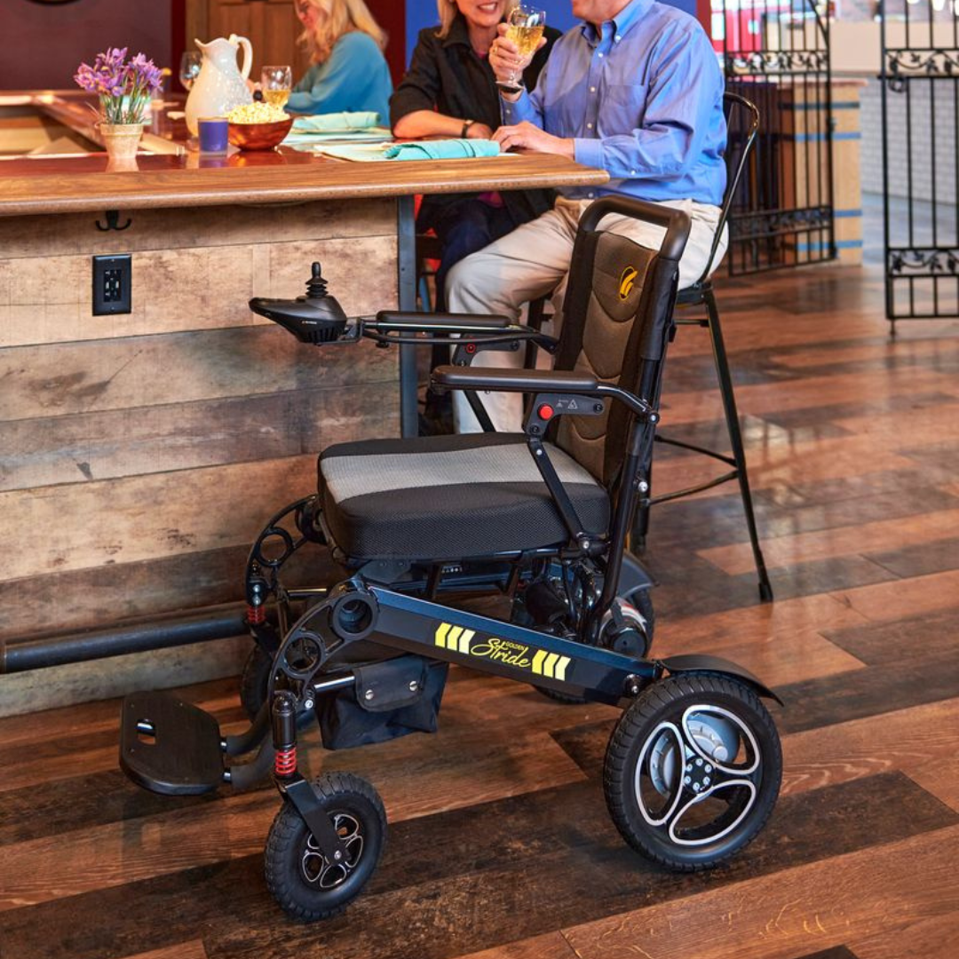 Golden Technologies Stride Folding Lightweight Electric Wheelchair on a wooden floor with people in the background
