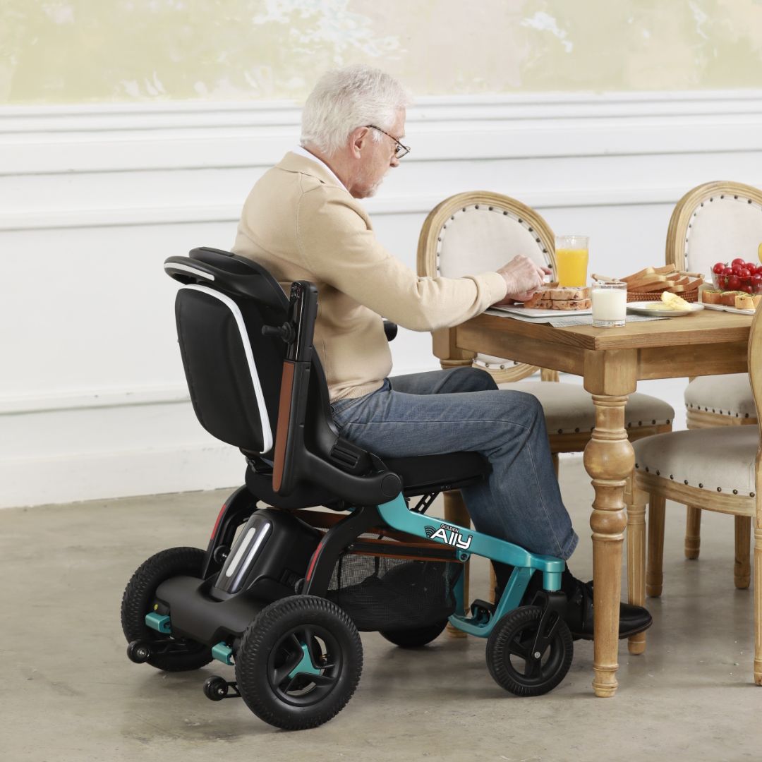 Man using a Golden Ally power wheelchair at a dining table with a meal.