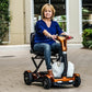 Woman using a EV Rider TEQNO folding mobility scooter in gold outdoors on a paved area.