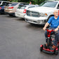 Man using a red EV Rider TEQNO folding mobility scooter in a parking lot with cars around