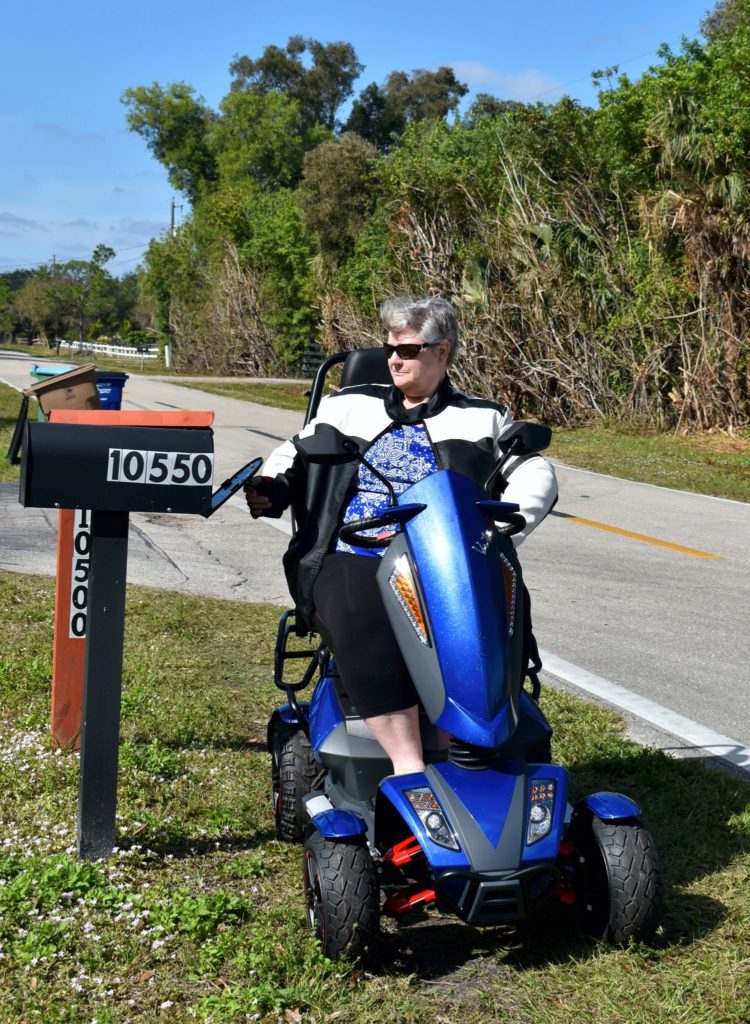 Person on a EV Rider Vita Monster Heavy-Duty Mobility Scooter in Blue by a mailbox with trees in the background