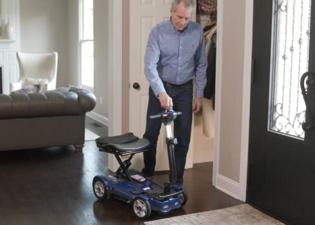 Man using EV Rider Transport 4AF Automatic Folding Travel Mobility Scooter in blue inside home