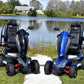 EV Rider Vita Monster Heavy-Duty Mobility Scooters on a grassy area near a body of water with trees in the background.