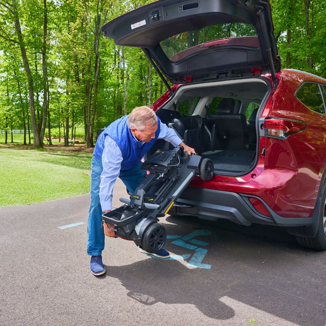Man loading a CarryOn HD  into the trunk of a red SUV in a park setting.