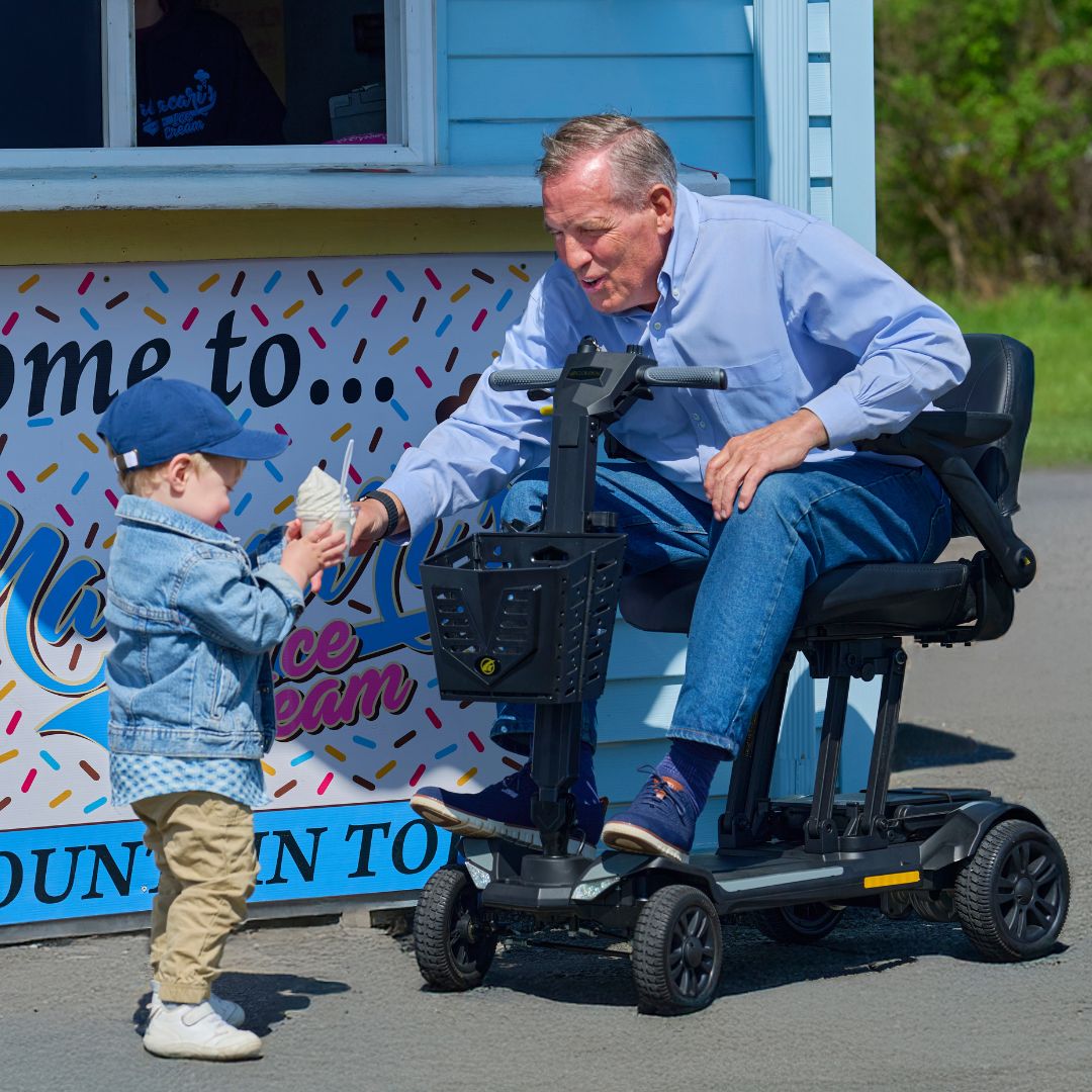 Man on a CarryOn HD mobility scooter interacting with a child in front of an ice cream truck.
