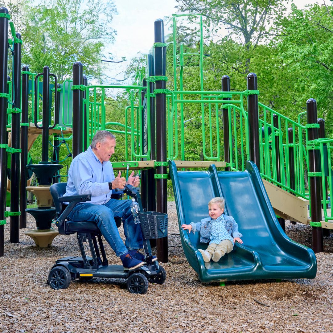 Man on a CarryOn HD mobility scooter interacting with a child at a playground.